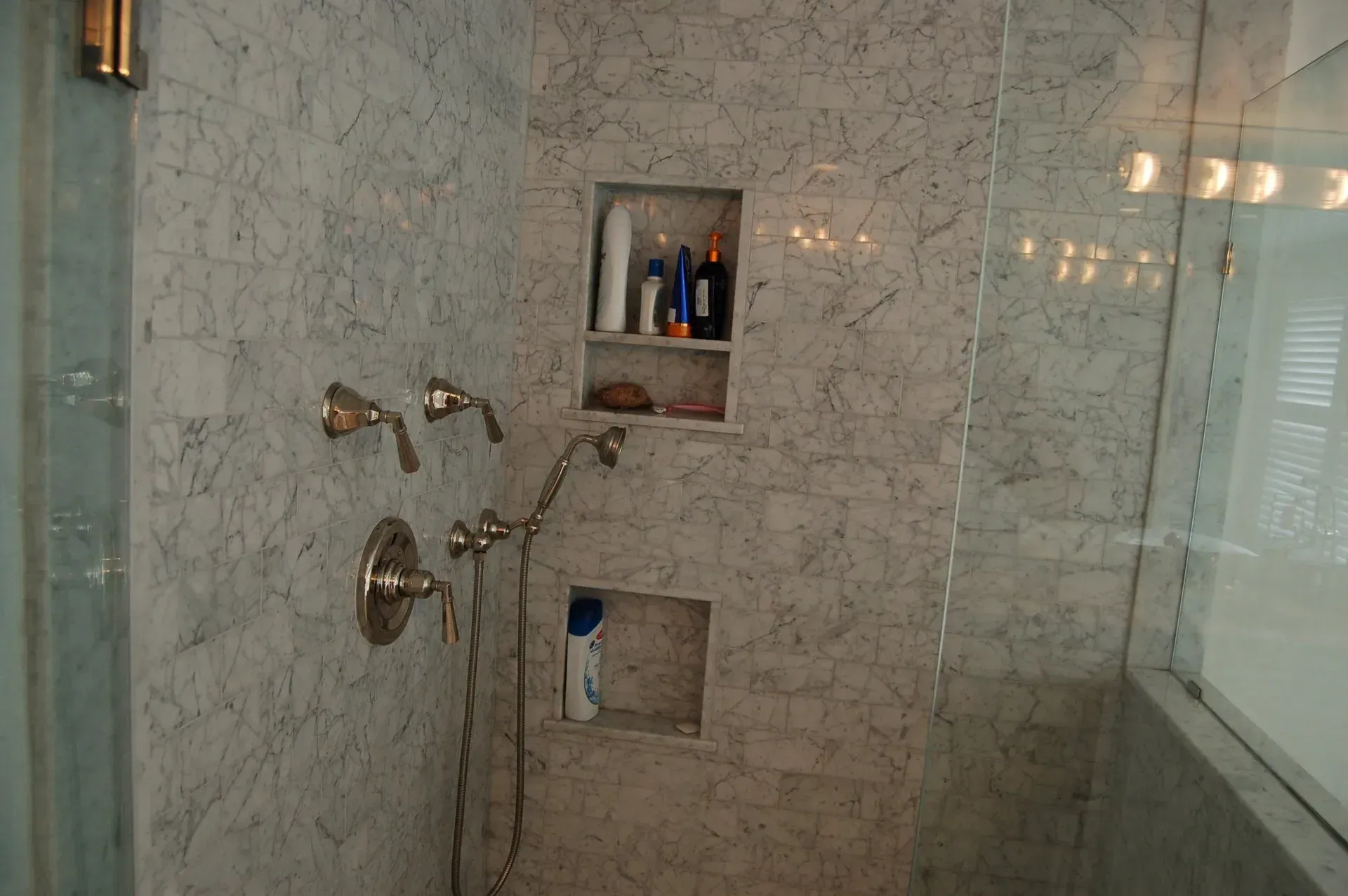 Shower with marble tile walls, niche shelves holding toiletries, and a glass door.