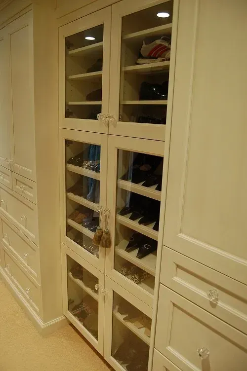Tall, cream-colored cabinet with glass doors displaying shoes on shelves.