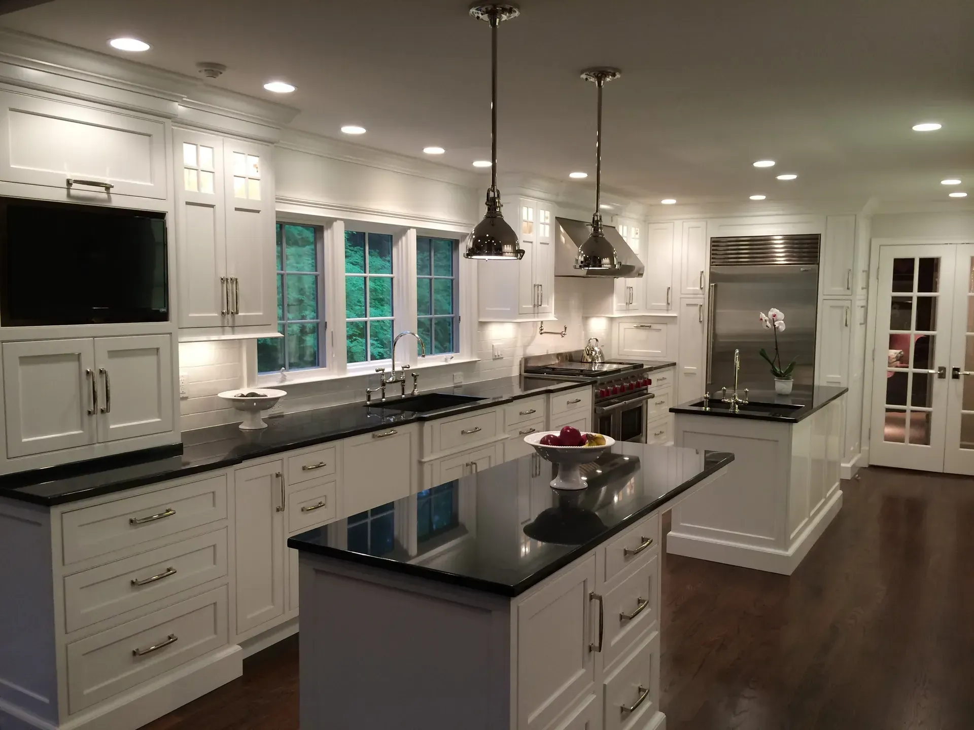White kitchen with black countertops, two islands, stainless steel appliances, and dark wood floor.