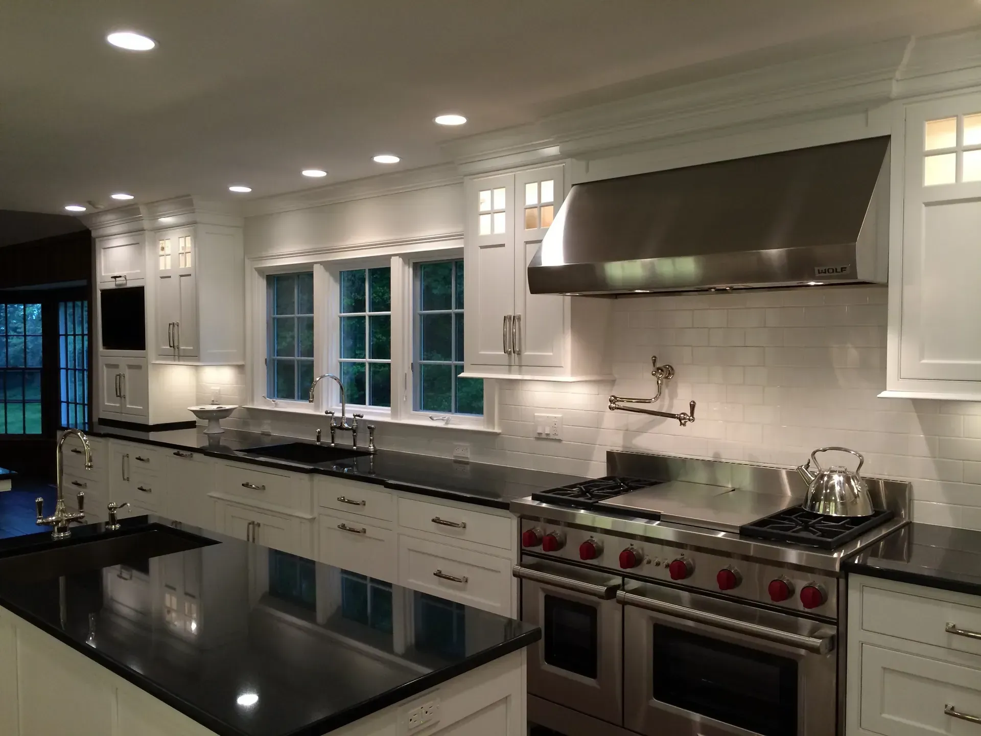 White kitchen with stainless steel appliances, black countertops, and recessed lighting.