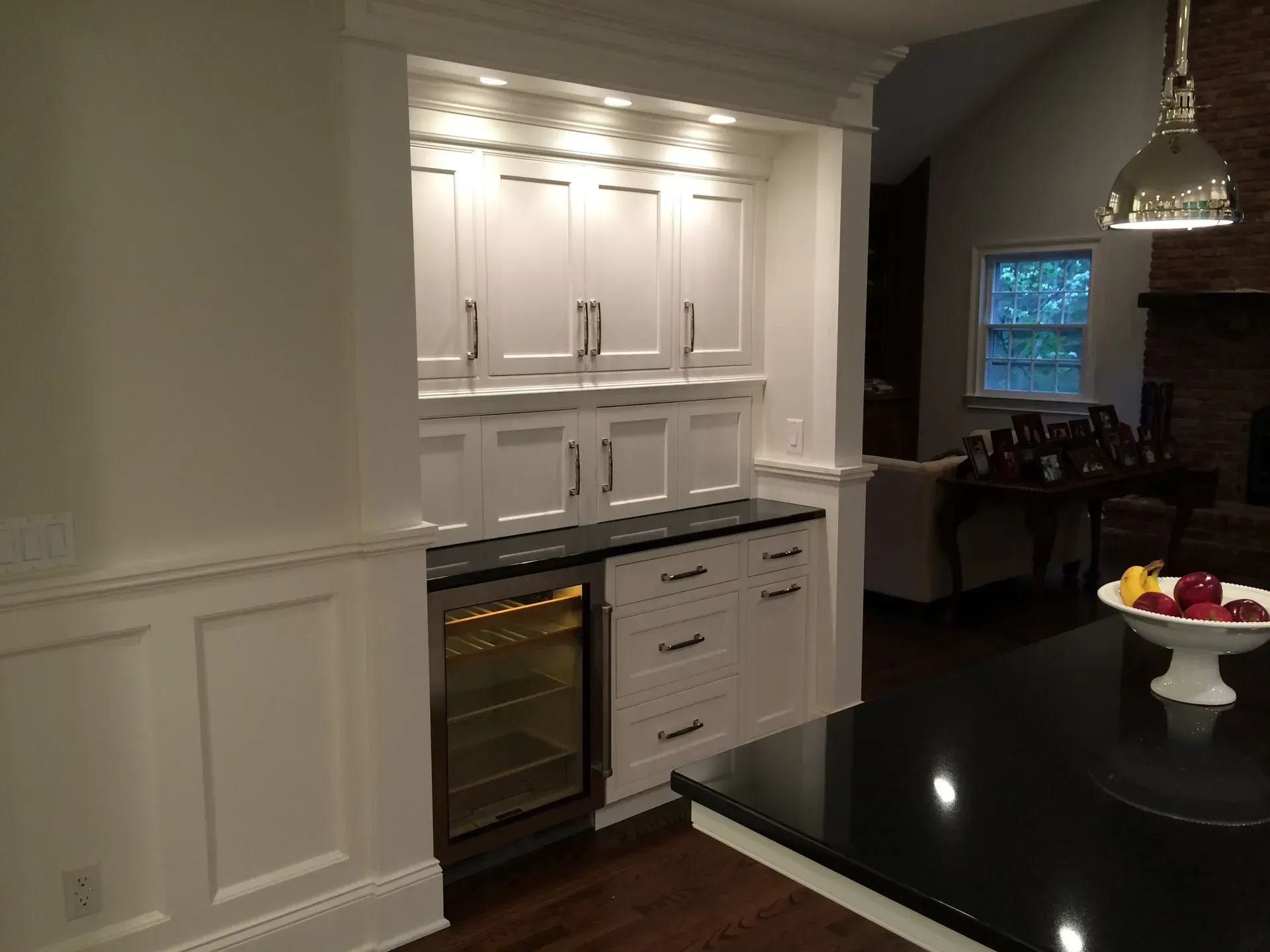 Built-in white cabinets with wine fridge and black countertop in a kitchen.