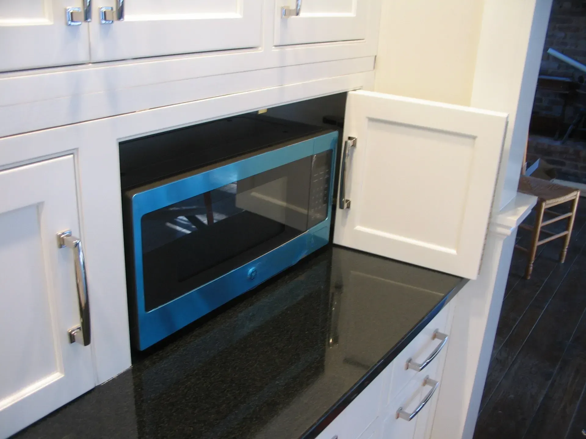 Blue microwave oven built into white kitchen cabinets. Door open to access.