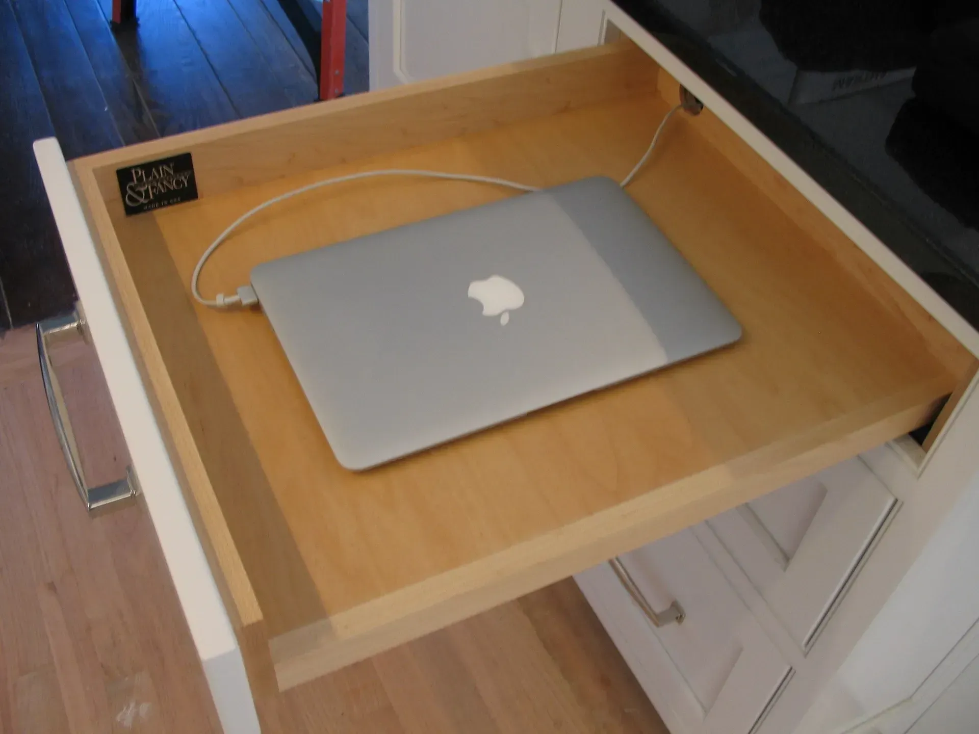 Opened kitchen drawer with a silver laptop inside; white cabinetry surrounds.