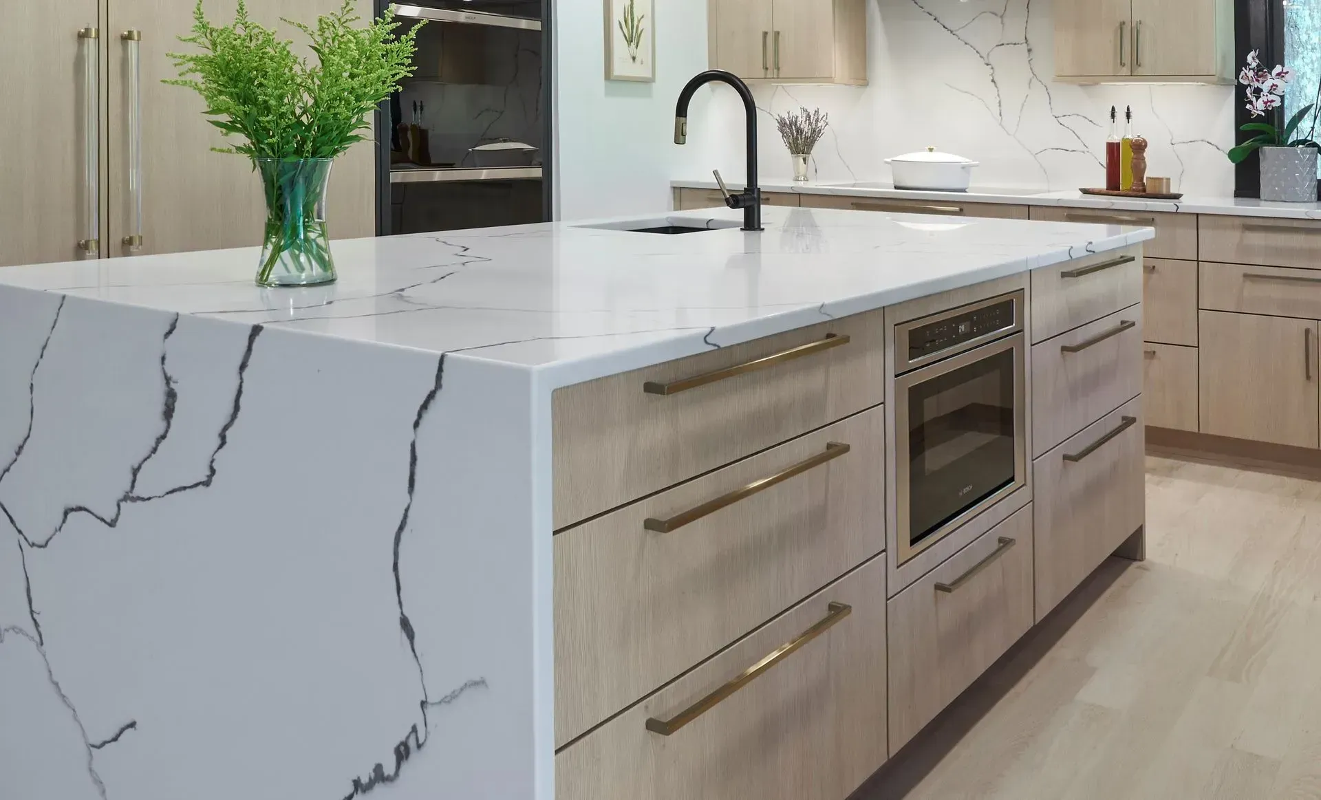 Modern kitchen island with quartz countertop, light wood cabinets, and built-in appliances.