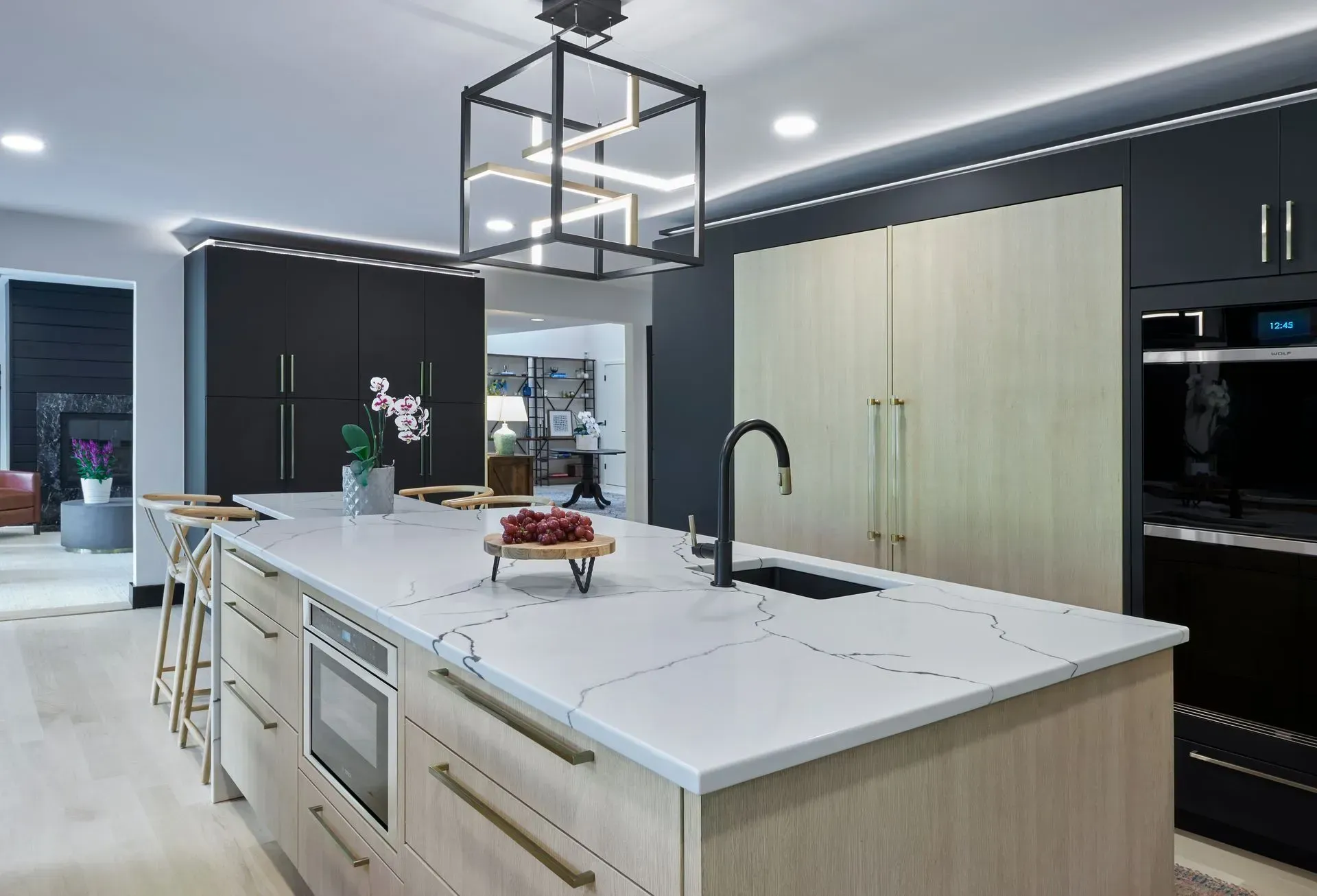 Modern kitchen with light wood island, dark cabinetry, and statement lighting.