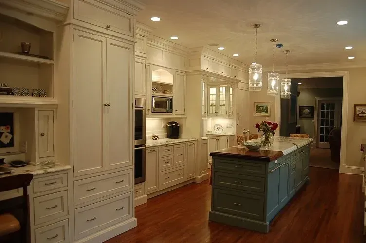Elegant kitchen with white cabinets, wood floors, and a teal island.