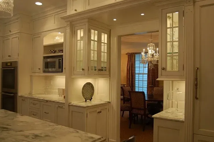 White kitchen with glass-front cabinets and a view into a dining room with a chandelier.