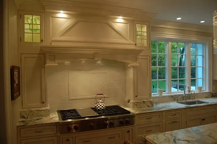Cream-colored kitchen with range, overhead hood, and countertop. Window with green outside view to the right.