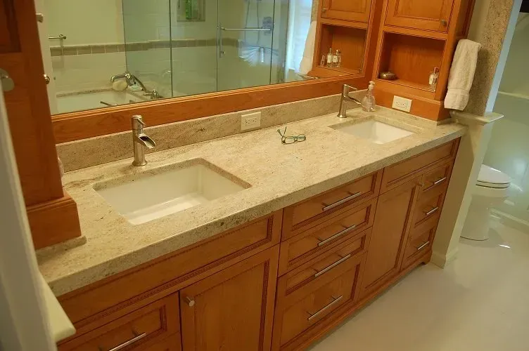 Bathroom vanity with two sinks, light granite countertop, and wooden cabinets.