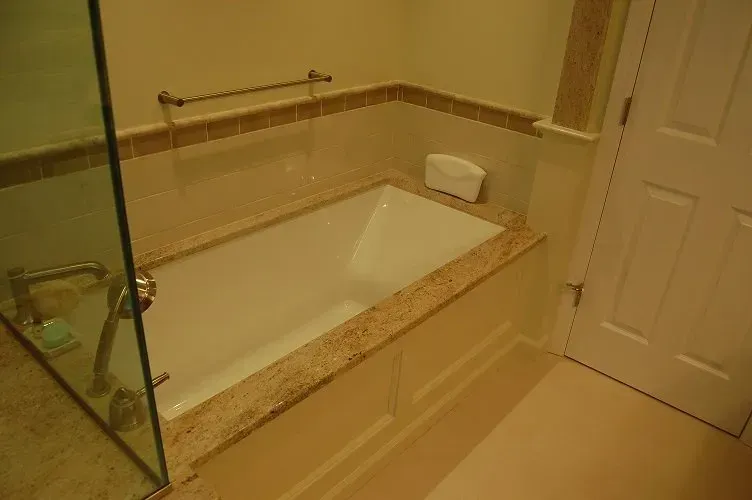 Bathroom with white bathtub, beige walls, and a glass shower door.