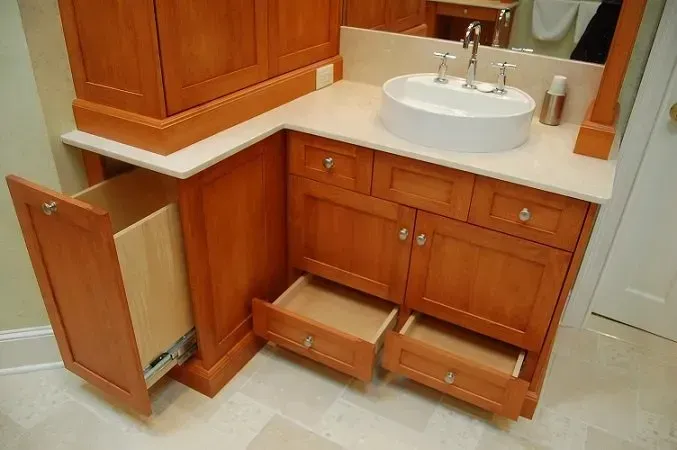 Bathroom vanity with open drawers and pull-out waste bin, tan countertop, orange cabinets, white sink.