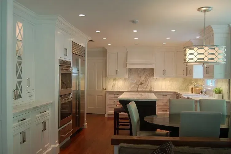 White kitchen with stainless steel appliances, marble backsplash, island, and dining area.