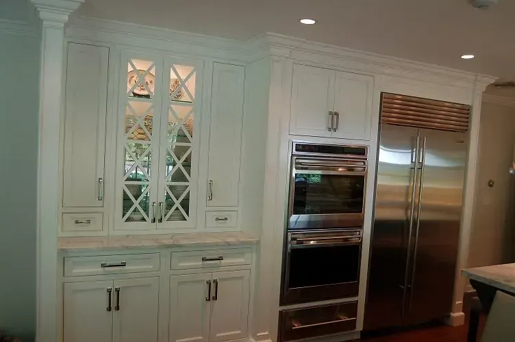 White kitchen cabinets with glass doors, oven, and stainless steel refrigerator.