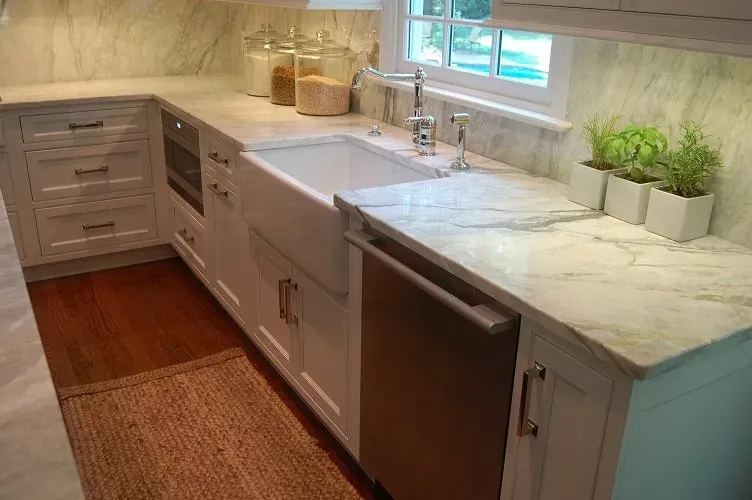 White kitchen with marble countertops, farmhouse sink, and stainless steel dishwasher.