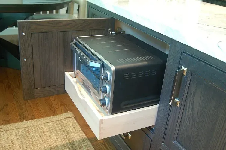 A black toaster oven on a pull-out drawer inside a dark wood cabinet.