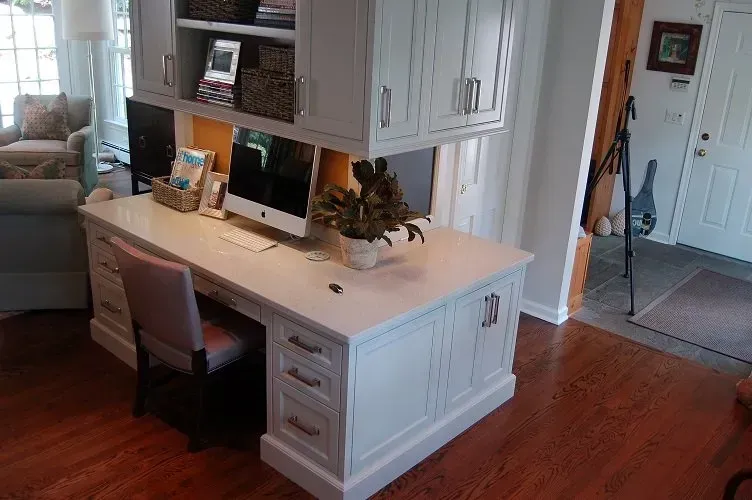 White home office desk with computers, cabinets, and a chair.