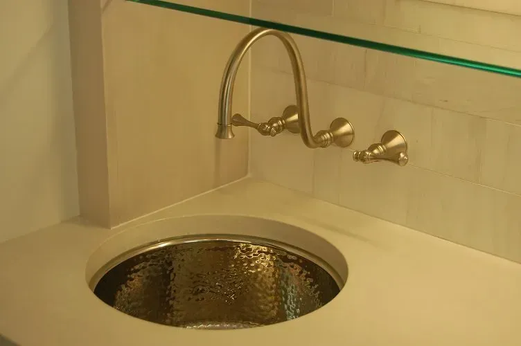 Gold-toned faucet over a hammered copper sink, set in a light-colored countertop.