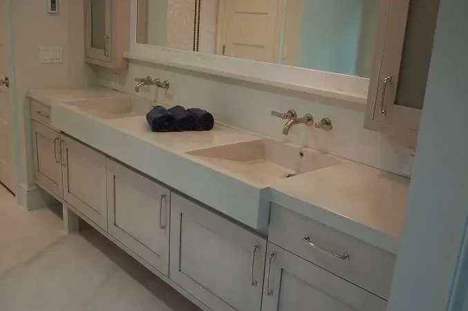 Bathroom vanity with two sinks, light cabinets, large mirror, and faucets, featuring rolled blue towels.