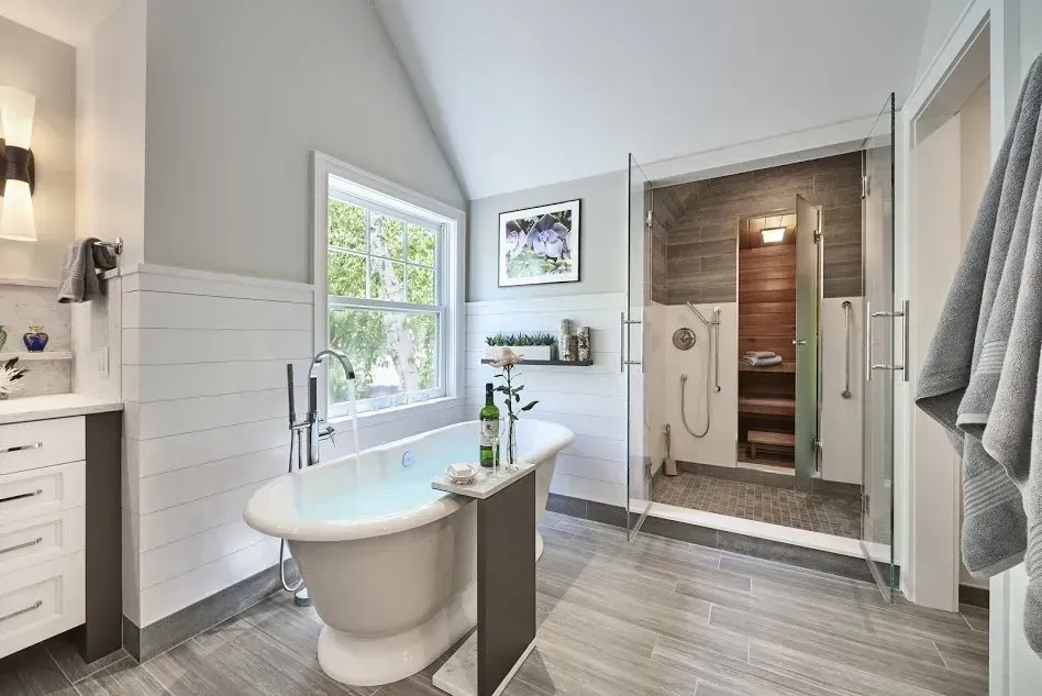 Bright bathroom with a white clawfoot tub, glass shower, and gray tile floor.