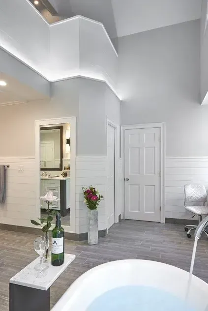 A spacious, modern bathroom with a white tub, gray floors, and a view into a second room.