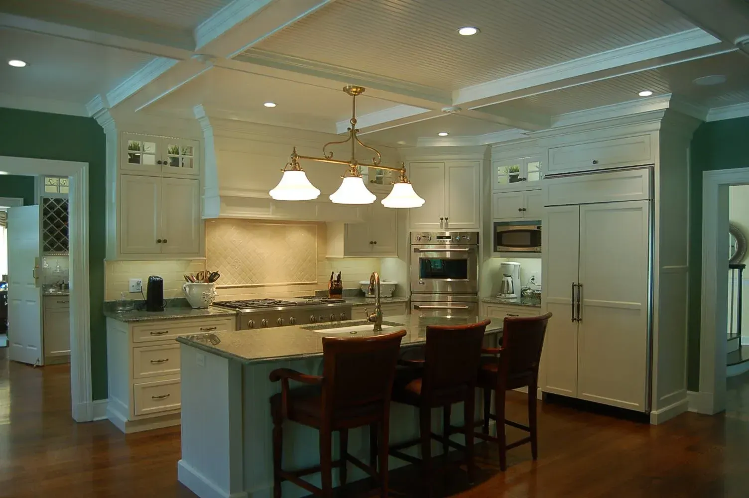 Bright, white kitchen with an island, cabinets, stainless steel appliances, and brown chairs.