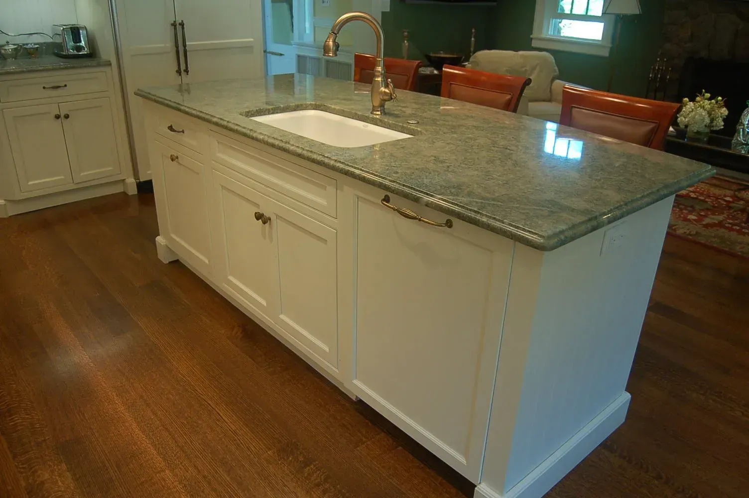 White kitchen island with a granite countertop, sink, and a gold faucet.