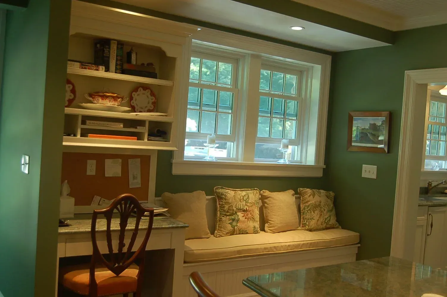 Cozy built-in bench seating with floral pillows and desk area beside windows in a green-walled room.