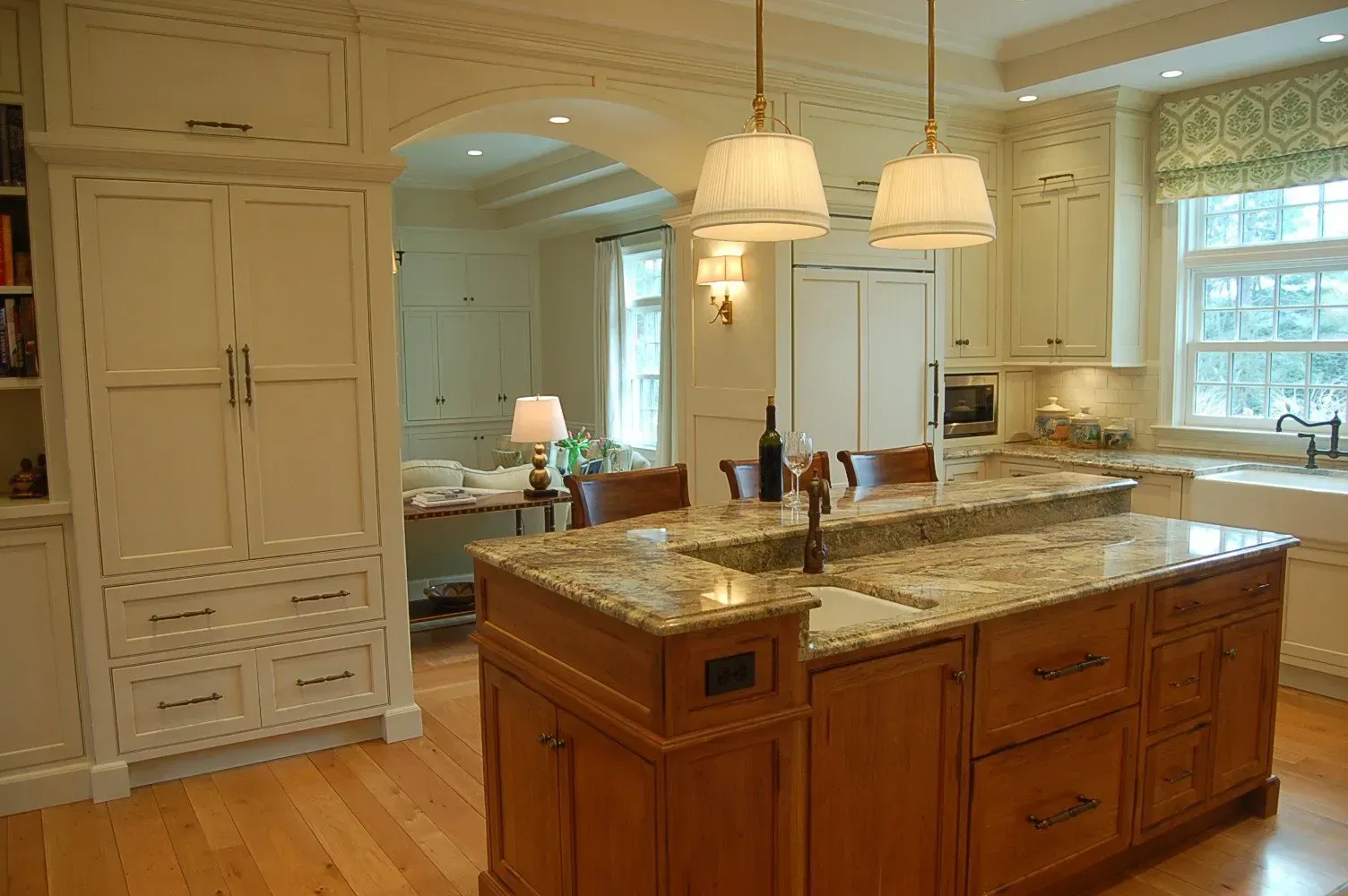 Elegant kitchen with cream cabinets, wooden island, granite countertop, pendant lights, and archway.