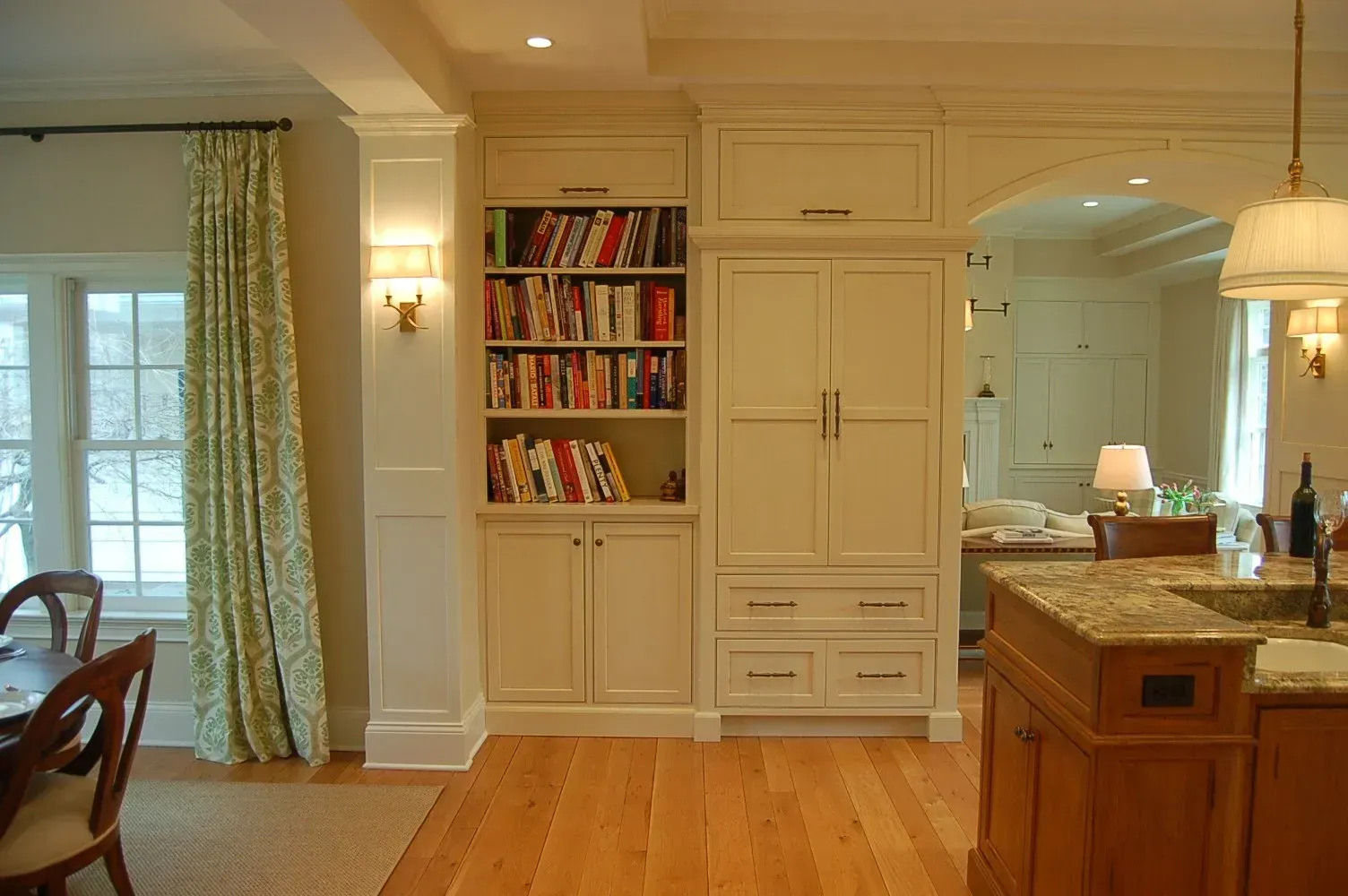 Cream-colored kitchen cabinets with a bookshelf, built-in refrigerator, and wood flooring.
