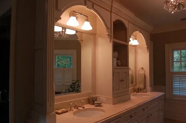 Bathroom vanity with arched mirrors, lighting, and cabinets, beige and white tones.