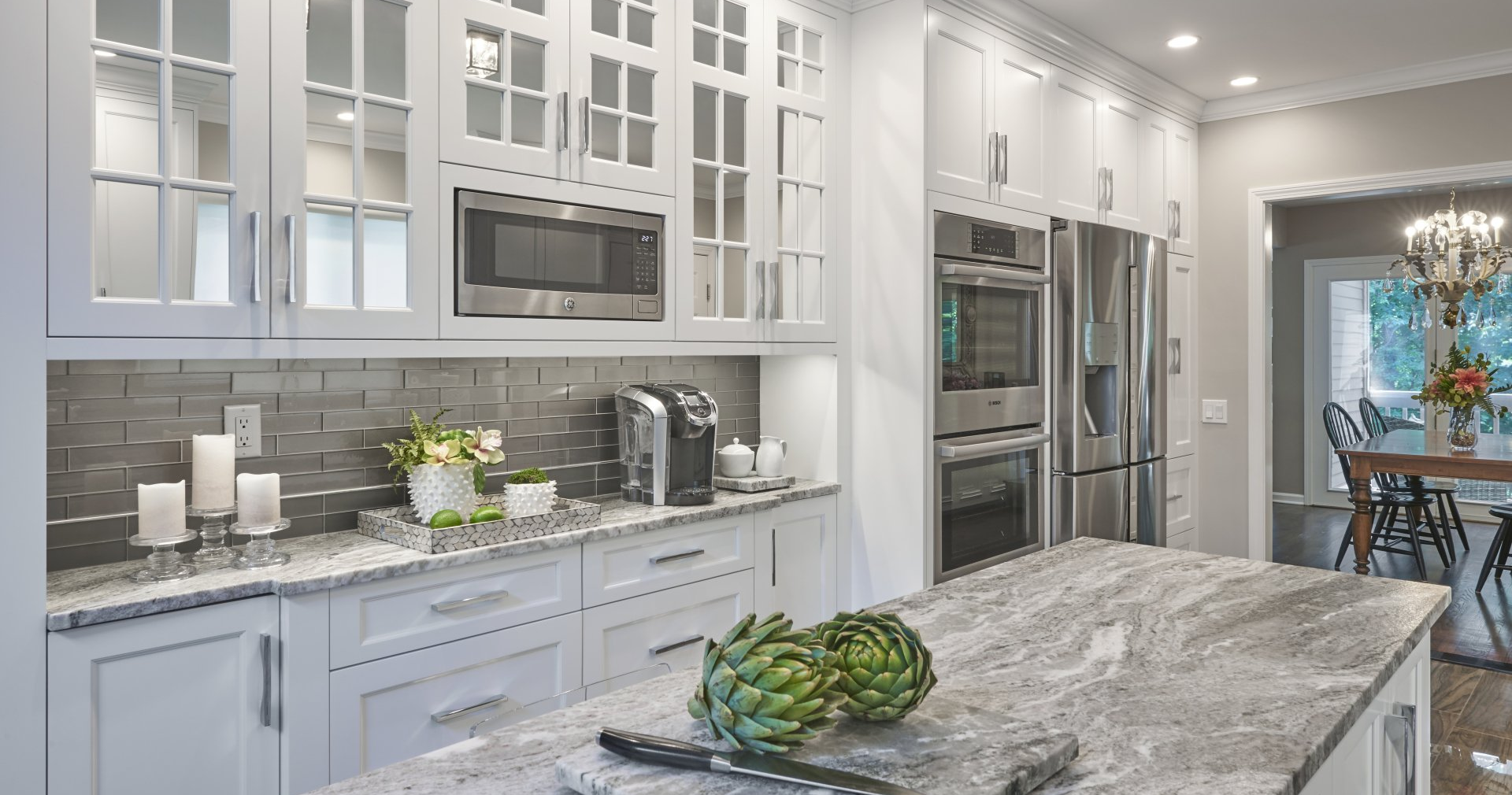 White kitchen with a large island, stainless steel appliances, and a gray backsplash.