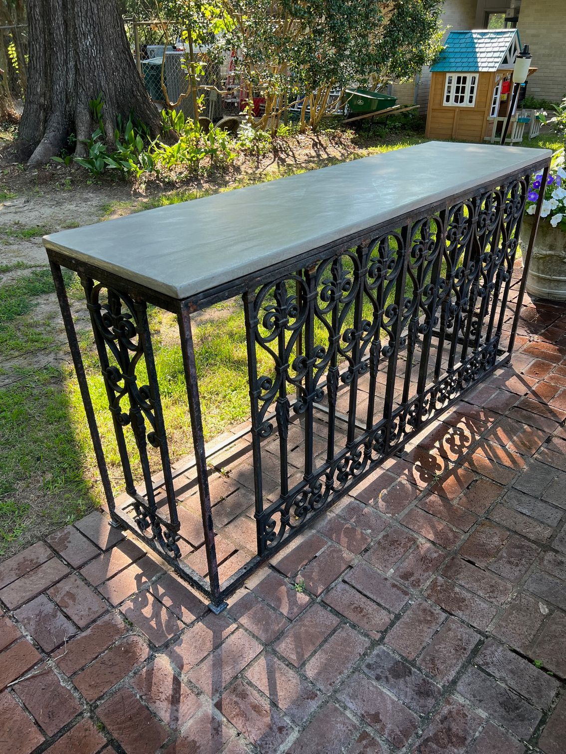 A long table with a wrought iron railing is sitting on a brick patio.