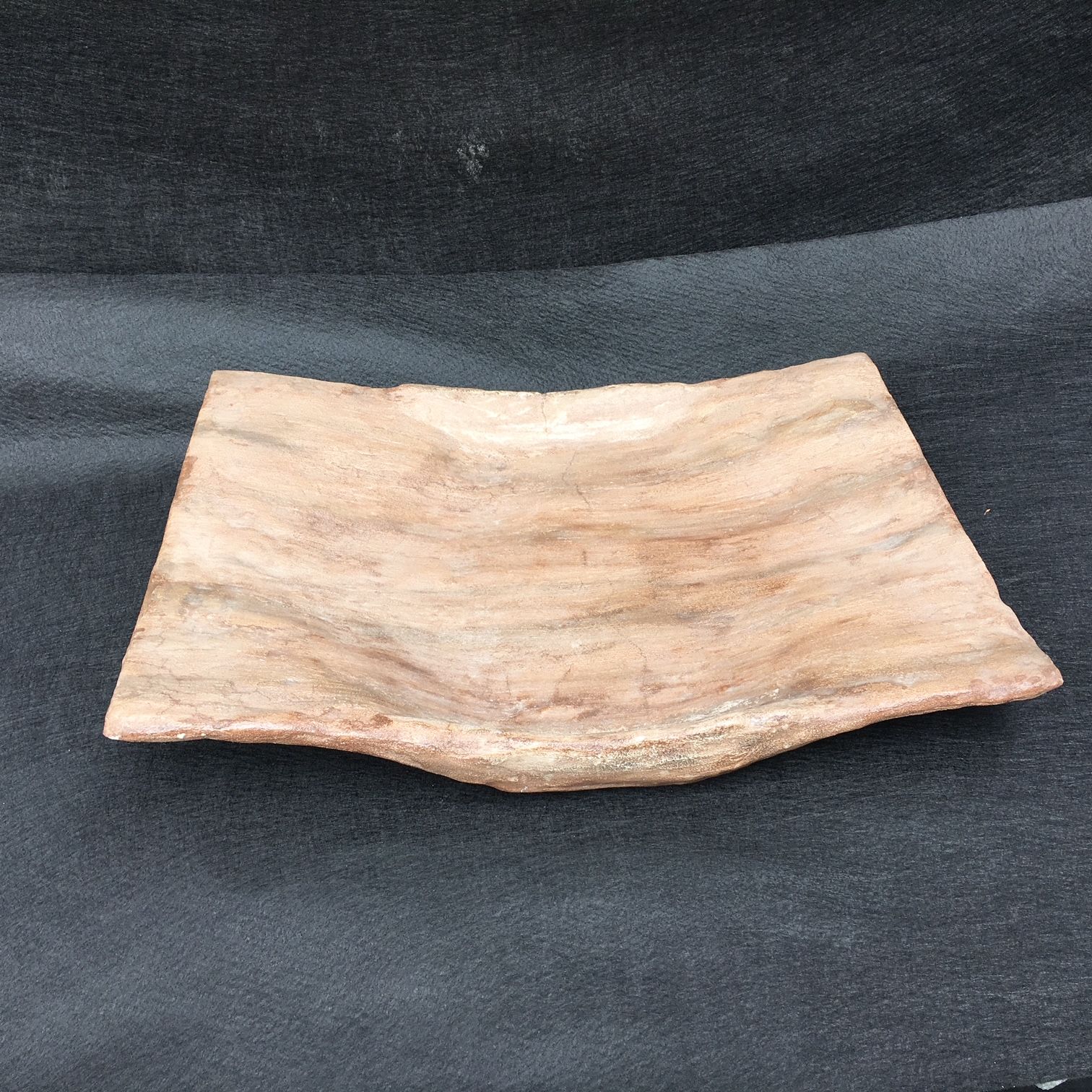 A wooden plate is sitting on a black cloth.