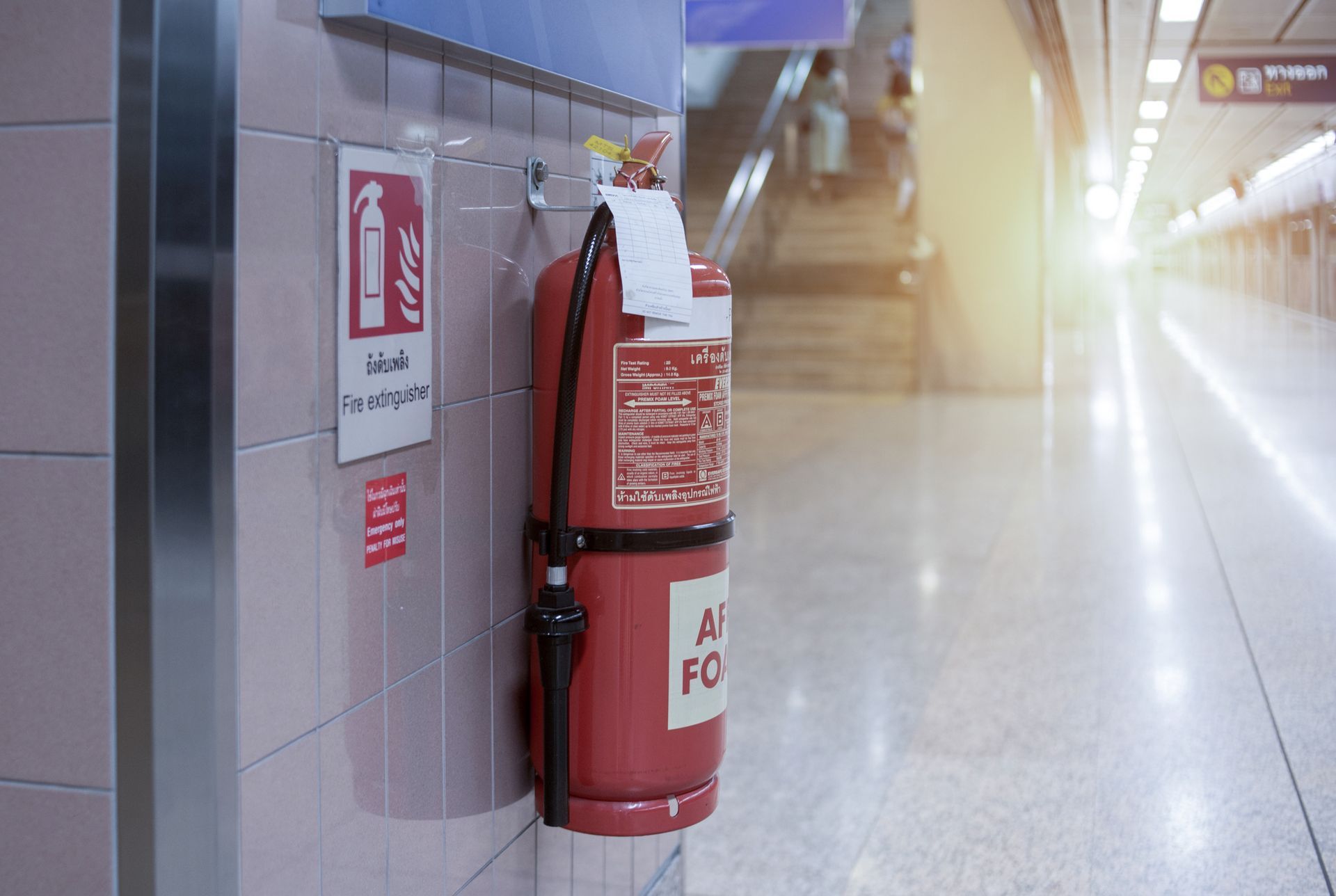A red fire extinguisher is hanging on a wall next to a sign.