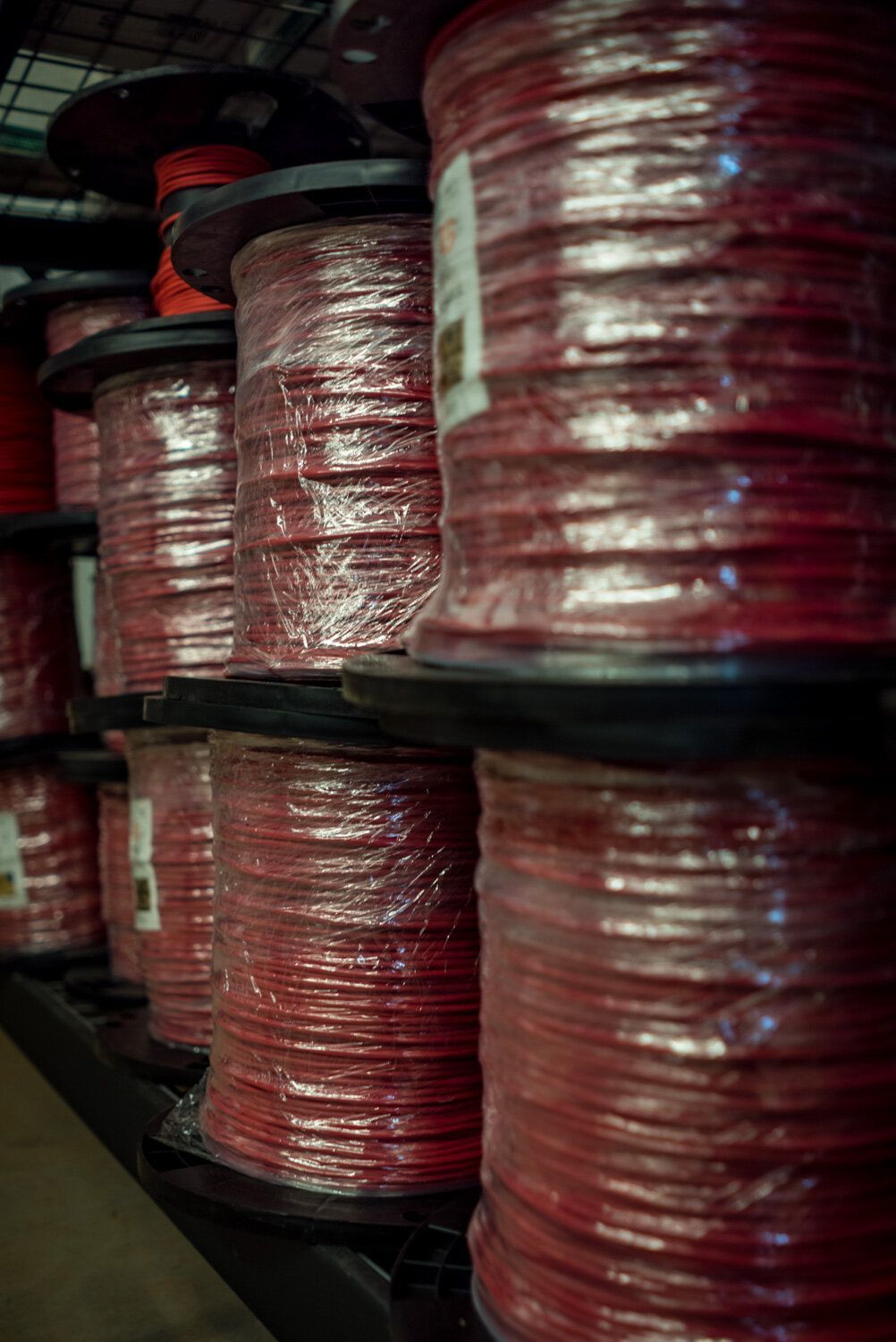 A bunch of spools of red wire are stacked on top of each other on a shelf.