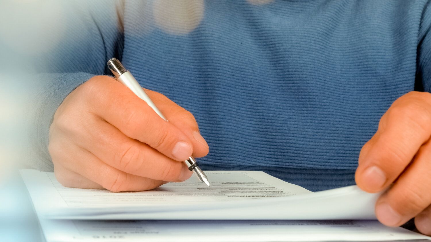 A person is writing on a piece of paper with a pen.