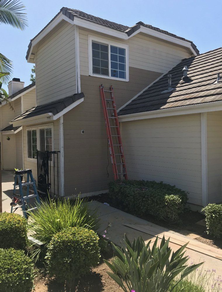 Two-story house exterior with a red ladder leaning against the wall and a garage on the right.