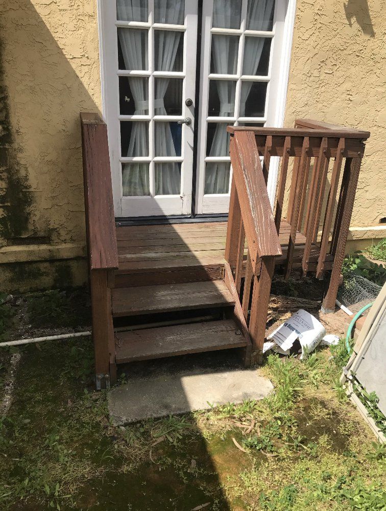 Small wooden steps and ramp beside a white French door on a beige house, with grass and sunlit shadows.