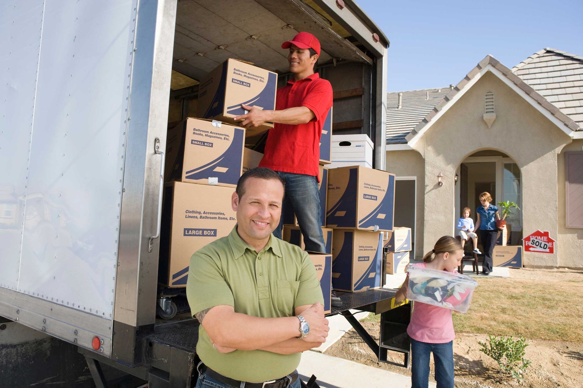 A family and a removalist are unloading a moving truck of cardboard boxes.