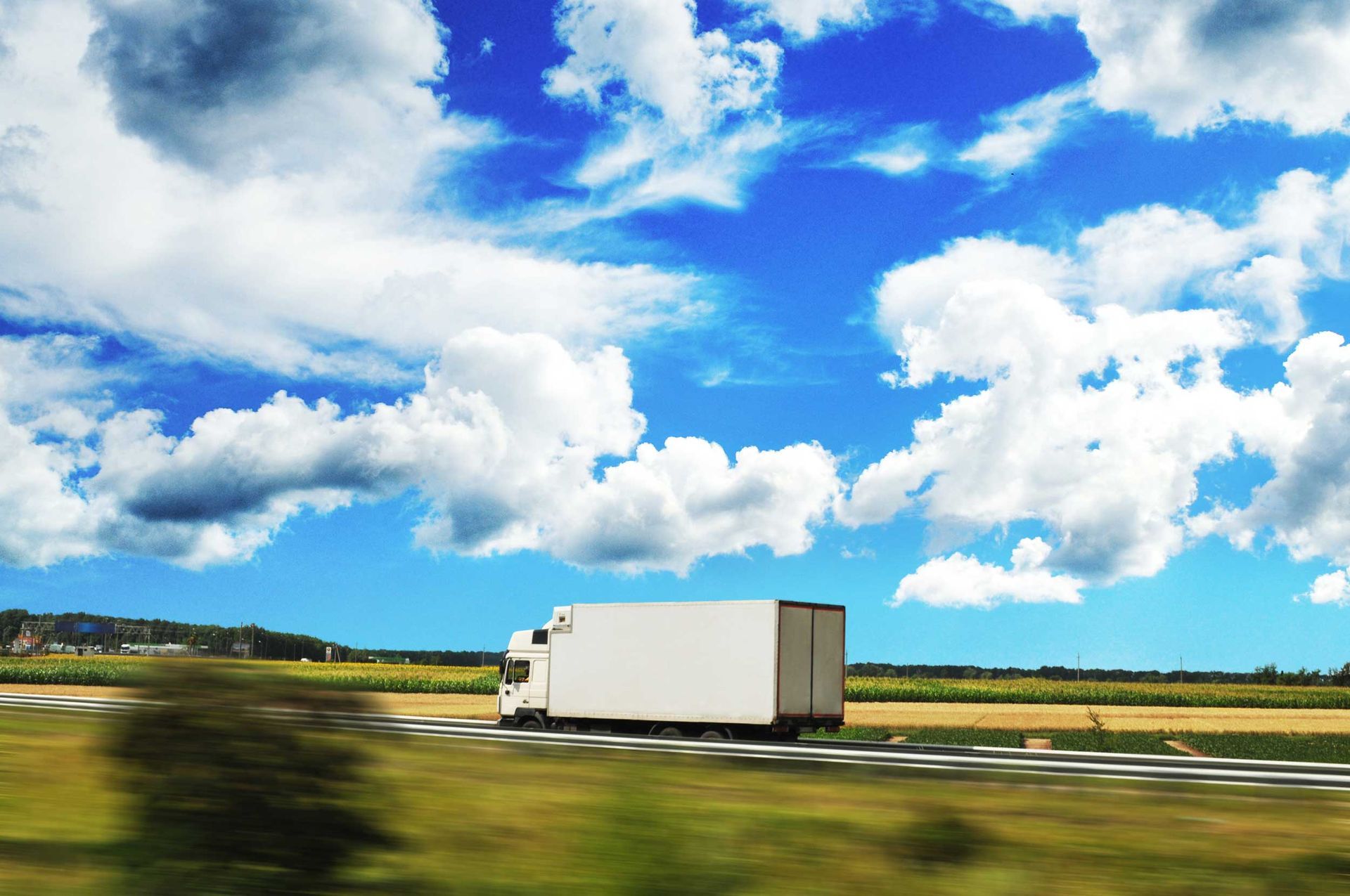 A box truck driving fast on a road against a blue sky with clouds. A box truck driving fast on a road against a blue sky with clouds.