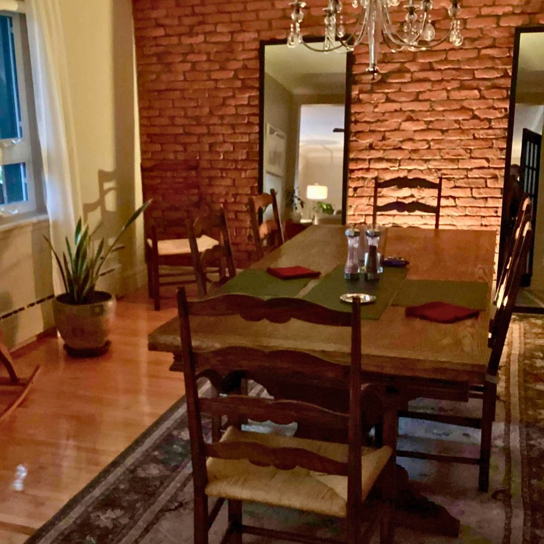 Salle à manger avec table en bois, mur de briques, lustre et chaises.