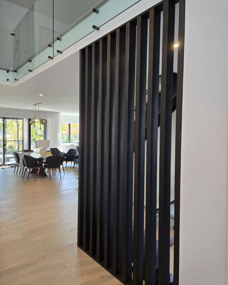 Cloison à lattes noires dans une maison moderne ; salle à manger ouverte en arrière-plan, parquet en bois clair.