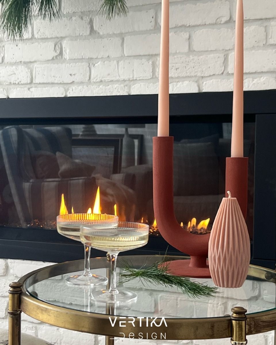 Deux coupes de champagne et une bougie décorative sur une table, avec des bougies allumées et une cheminée en arrière-plan.