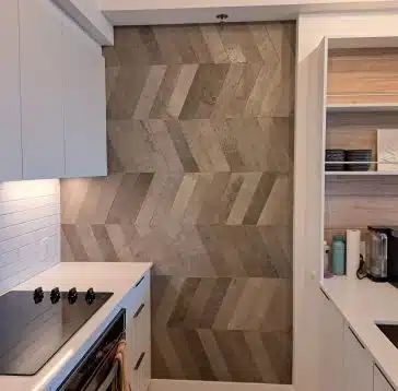 Cuisine moderne avec armoires blanches, table de cuisson noire et mur d'accent à motifs imitation pierre.