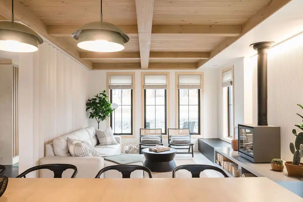 Séjour avec poutres apparentes en bois clair, murs blancs et mobilier moderne.