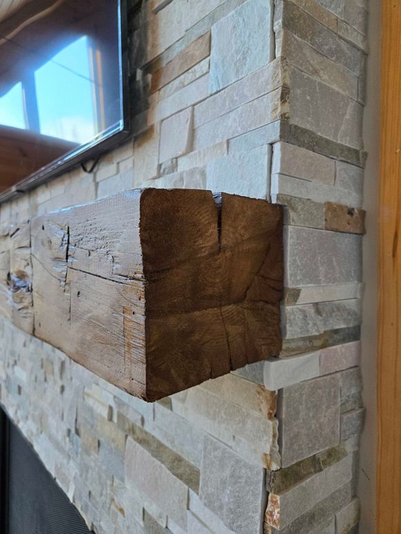 Cheminée en pierre avec insert et manteau noirs. Aménagement intérieur avec parquet et décoration en bois.