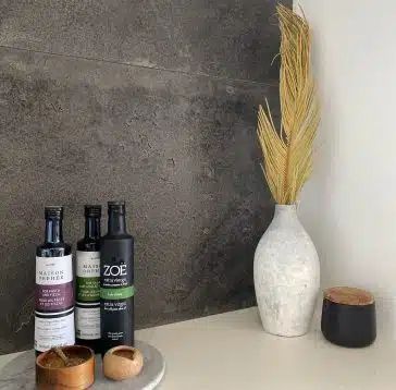 Bouteilles d'huile d'olive et vase avec des fleurs séchées sur un comptoir à côté d'un mur de pierre sombre.