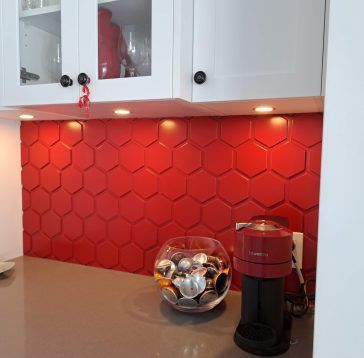 Dosseret en carrelage hexagonal rouge dans la cuisine avec armoires blanches et cafetière.