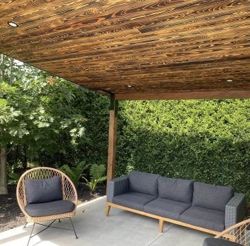 Terrasse aménagée sous un auvent en bois, avec vue sur une végétation luxuriante.
