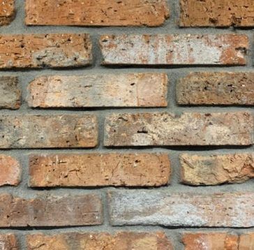 Gros plan d'un mur de briques. Briques brun-rouge aux textures variées, posées en appareillage continu avec du mortier gris.